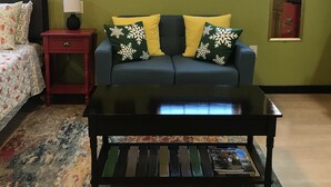A living room with a blue sofa, yellow and green pillows, a red nightstand, a black coffee table, and a patterned rug. - Cozy Efficiency Studio/A near DownTown (San Antonio)
