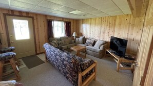 Ein gemütliches Wohnzimmer mit einer gemusterten Couch, einem kleinen Couchtisch, einem Fernseher auf einem Schrank und einer Holzvertäfelung.