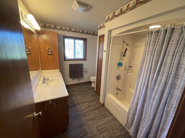 Une salle de bain avec un meuble-lavabo en bois, une baignoire et un rideau de douche.