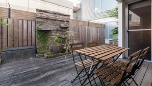 En udendørs terrasse med et træbord og stole, en stenvæg og et træhegn.