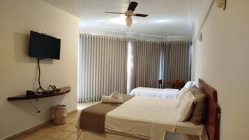 A hotel room with a bed, a television, a ceiling fan, and a window with curtains.