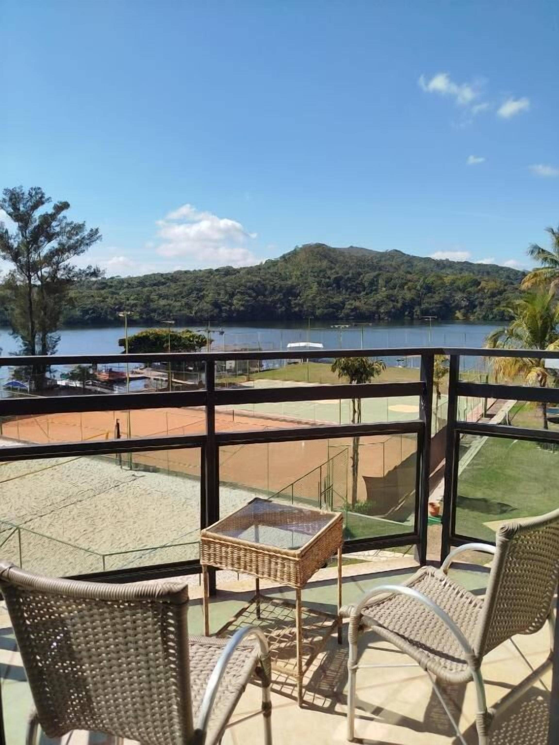 A balcony with wicker furniture overlooking a beach and a lake.