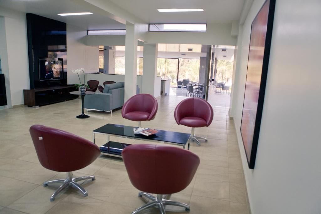 A modern waiting area with red chairs, a flat-screen TV, and a dining area in the background.
