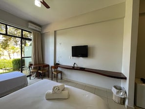 Habitación de hotel con cama, escritorio, televisión y ventana con cortinas.