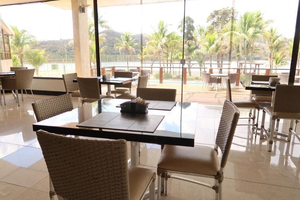 Un comedor con mesas y sillas, ventanas amplias y vistas a palmeras y una masa de agua.