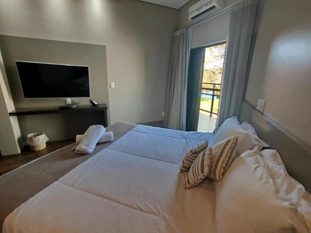 Habitación de hotel con una cama grande, un televisor de pantalla plana, una mesita y un ventanal con cortinas.