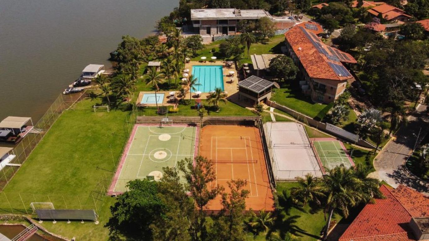 Ovenudblik over en ejendom med swimmingpool, tennisbaner og en bygning med rødt tag.