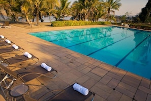 Una piscina con sillas de descanso y toallas, rodeada de palmeras y un cielo despejado.