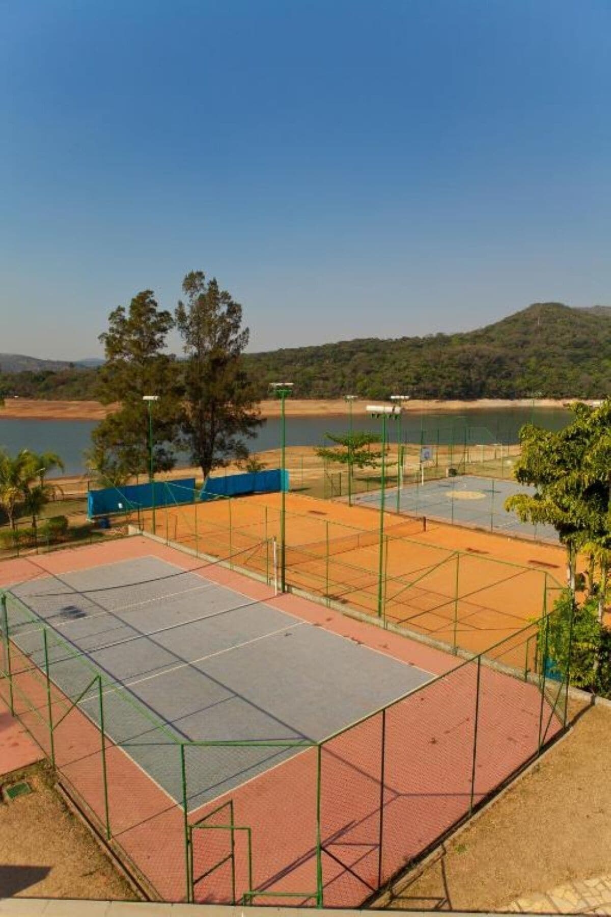 Una cancha de tenis con una red, rodeada por una cerca, y un cuerpo de agua al fondo.