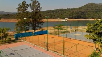 Una cancha de tenis con una red, rodeada por una cerca, y un cuerpo de agua al fondo.