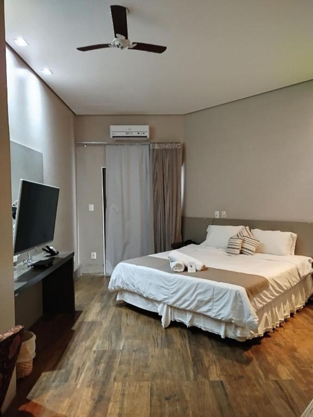 Ein Hotelzimmer mit einem Bett, einem Schreibtisch mit Computer, einem Deckenventilator und einer Klimaanlage.