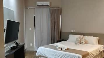 Ein Hotelzimmer mit einem Bett, einem Schreibtisch mit Computer, einem Deckenventilator und einer Klimaanlage.