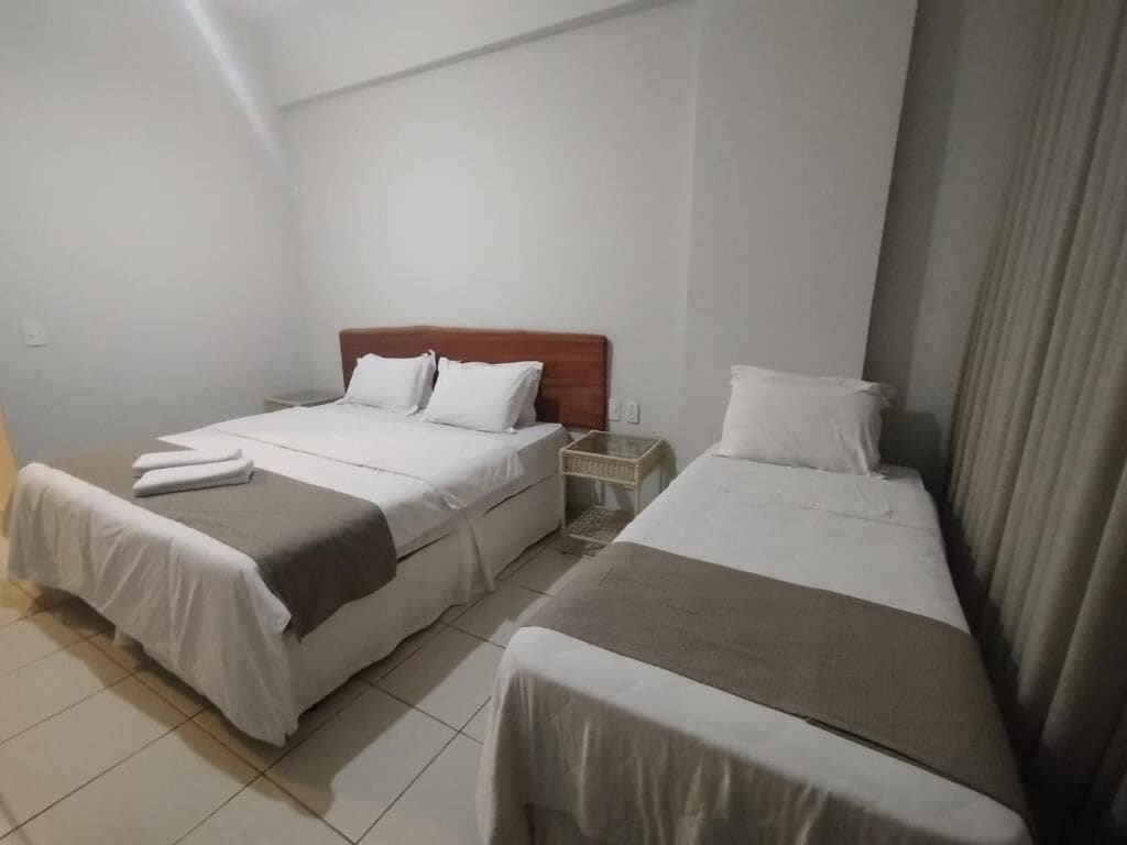 Habitación de hotel con dos camas individuales, cabecera de madera, mesita de noche y cortina.