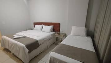 Habitación de hotel con dos camas individuales, cabecera de madera, mesita de noche y cortina.