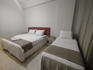 Habitación de hotel con dos camas individuales, cabecera de madera, mesita de noche y cortina.