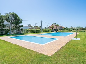 A rectangular outdoor swimming pool with a tiled deck, surrounded by well-maintained grass and trees.