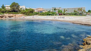 A beach resort with clear blue waters, sun loungers, and a large hotel building in the background. - Dream vacations in front of the Mediterranean Sea (L'Ametlla de Mar)