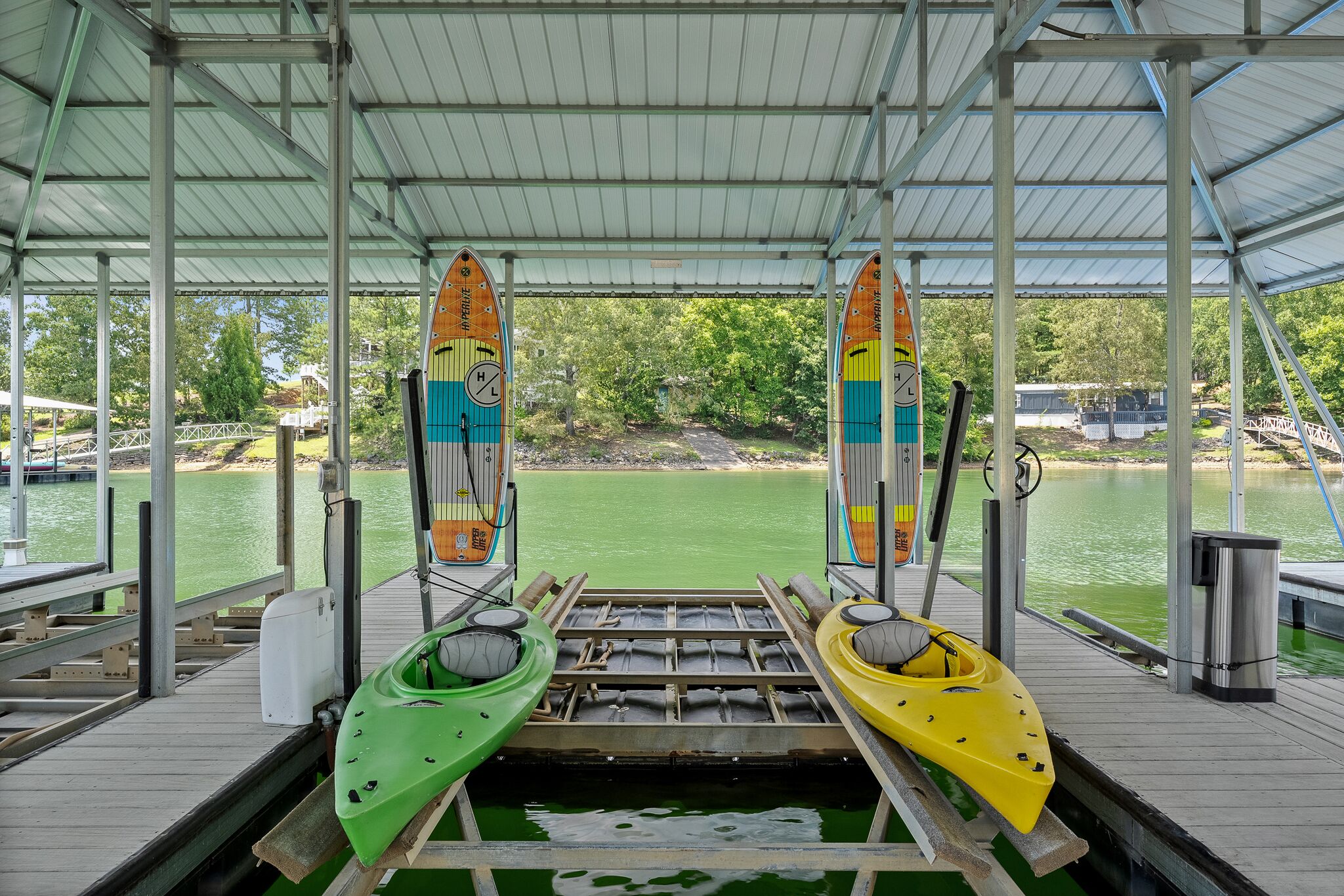 Un muelle cubierto con dos kayaks, una barandilla metálica y vistas a un lago y árboles.