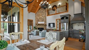 A spacious living area with a stone fireplace, wooden ceiling beams, and a dining table set for four. - Luxurious French Country Estate on Smith Lake- Flat yard, dock, fiber internet! (Arley)