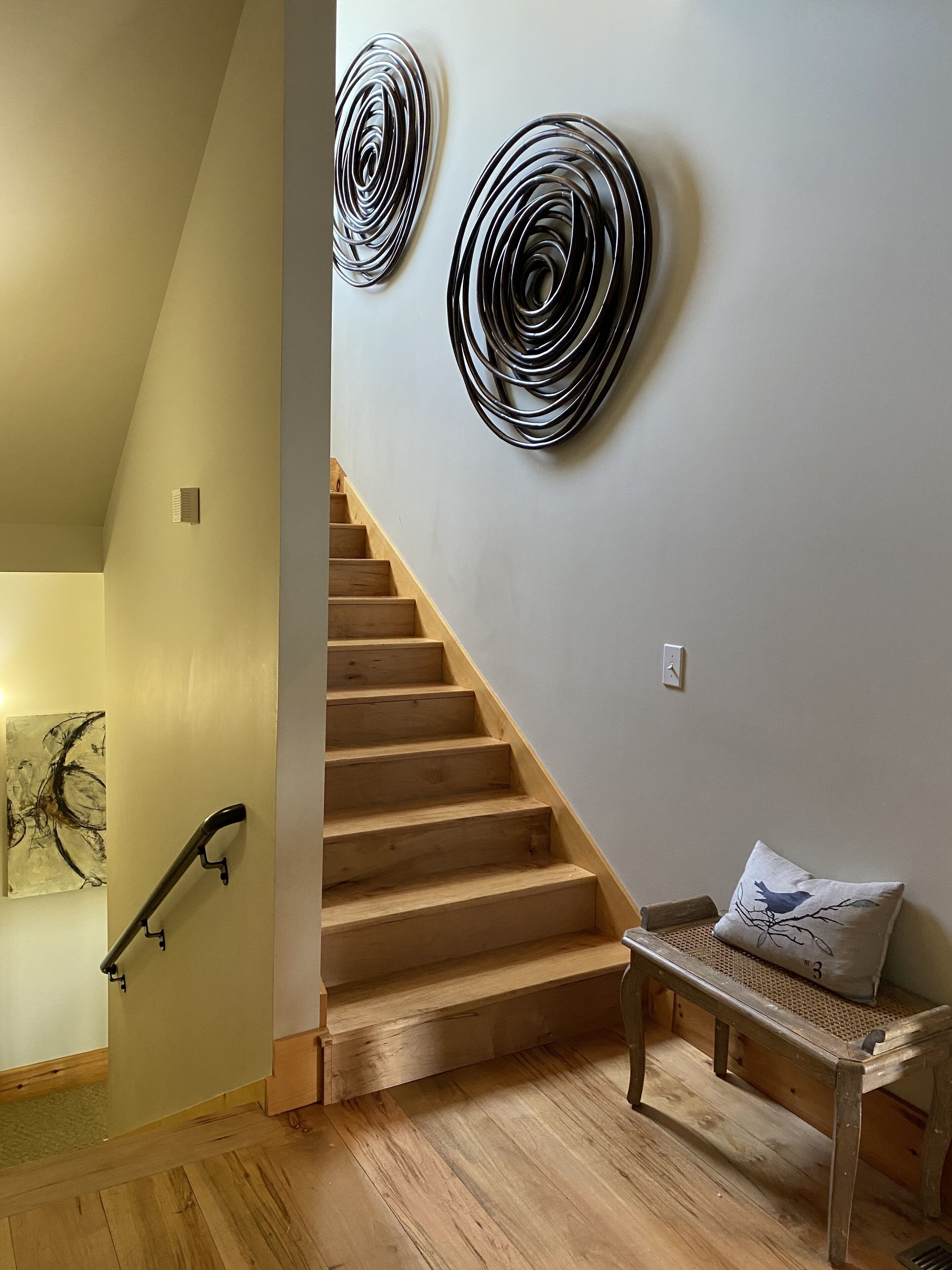 A staircase with wooden steps and a handrail, a wall-mounted abstract art piece, and a bench with a cushion.