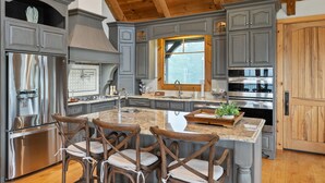 A modern kitchen with grey cabinetry, stainless steel appliances, and a large island with bar stools. - Luxurious French Country Estate on Smith Lake- Flat yard, dock, fiber internet! (Arley)