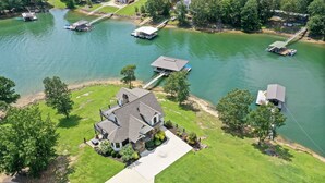A large house with a dock extending into a lake, surrounded by lush greenery and other houses. - Luxurious French Country Estate on Smith Lake- Flat yard, dock, fiber internet! (Arley)