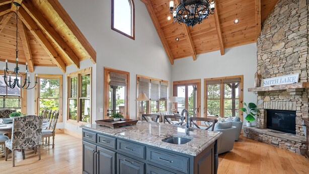 A spacious kitchen with a large island, wooden beams on the ceiling, and a stone fireplace. - Luxurious French Country Estate on Smith Lake- Flat yard, dock, fiber internet! (Arley)