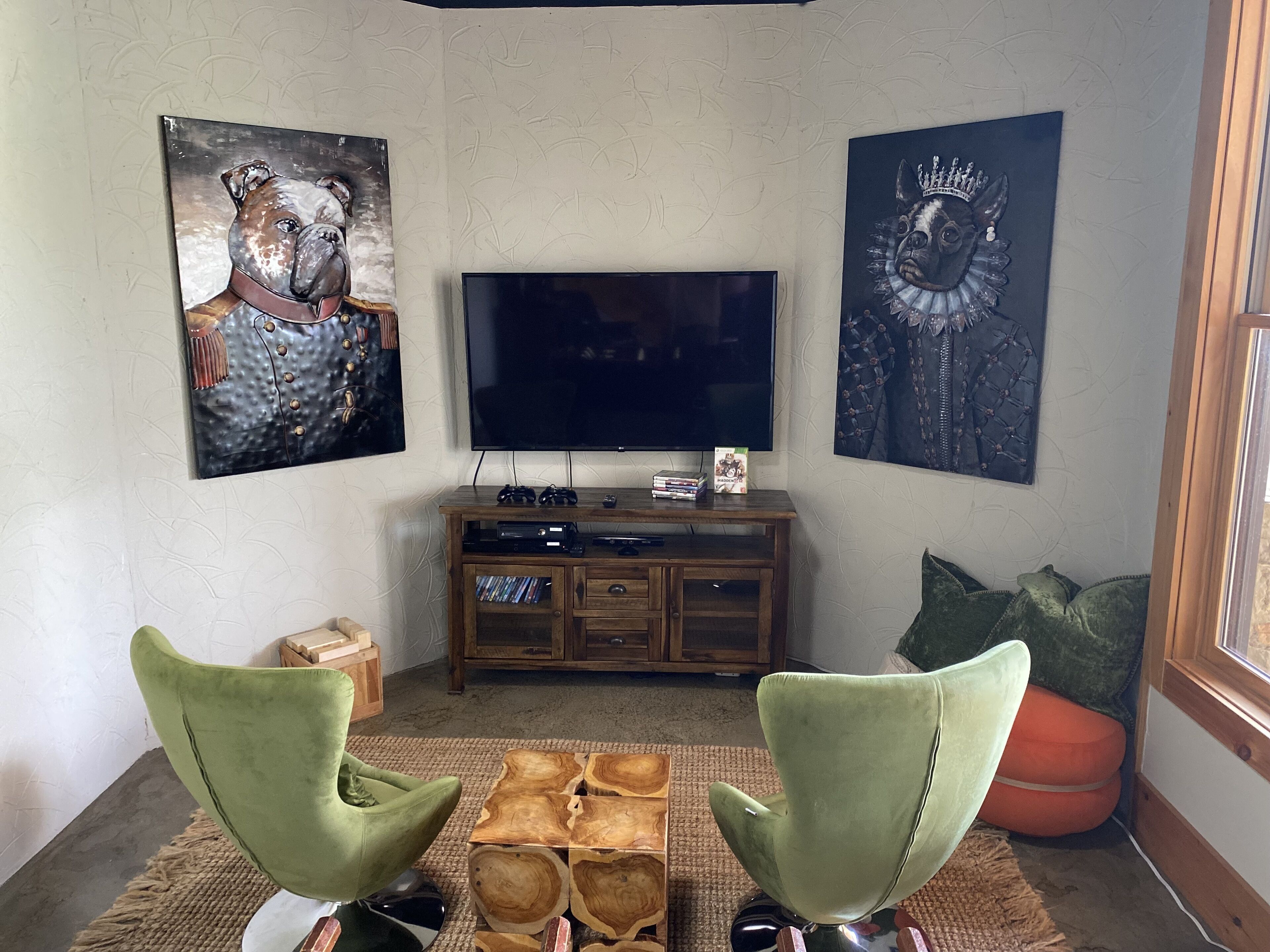 A living room with a TV, wooden entertainment unit, two green chairs, and artwork on the walls.