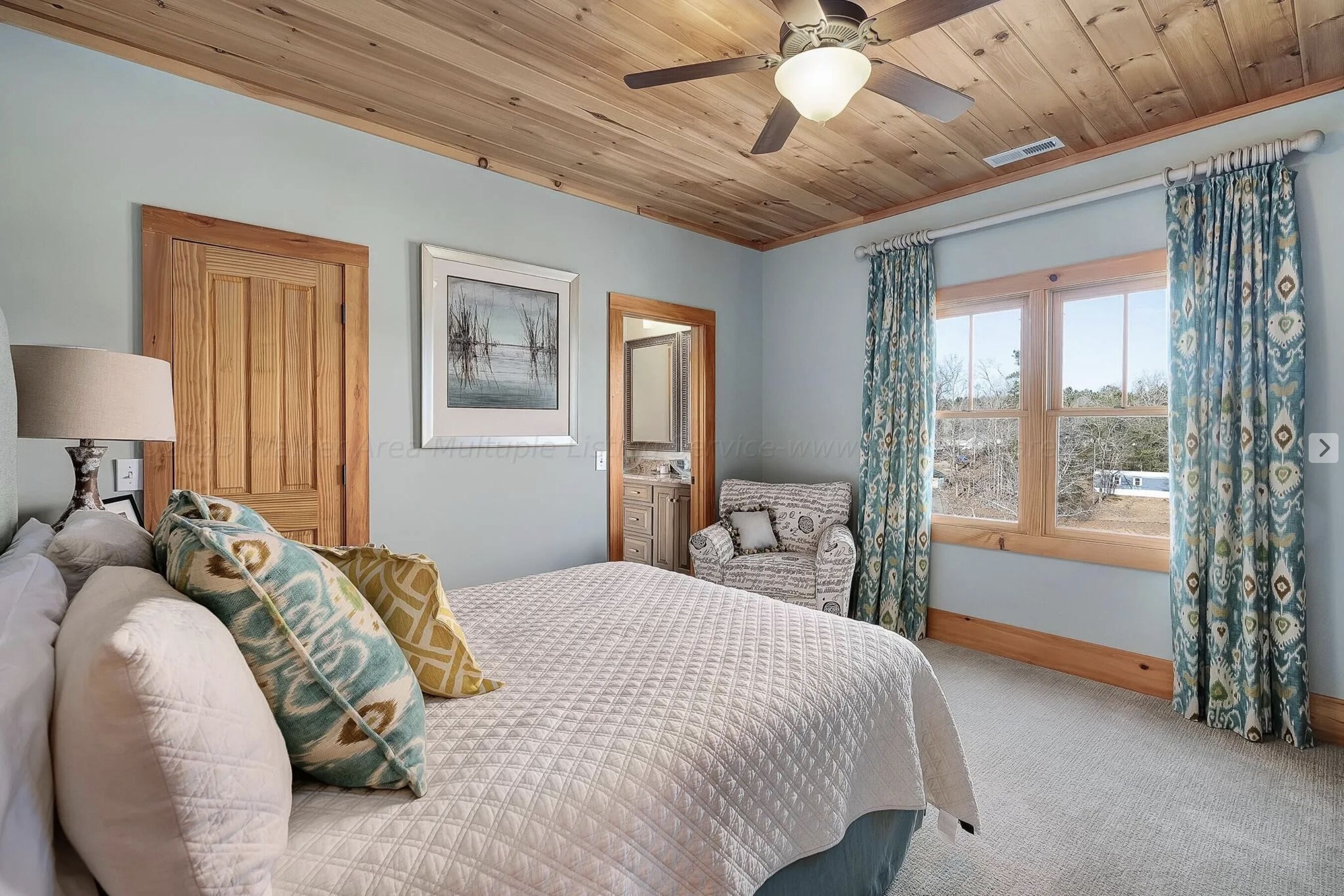 Une chambre à coucher avec un lit, une chaise, un ventilateur de plafond et une fenêtre avec des rideaux.