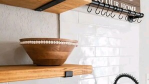 Una cocina con estantes de madera, un letrero de bienvenida, un bol, una planta en maceta y un lavabo.