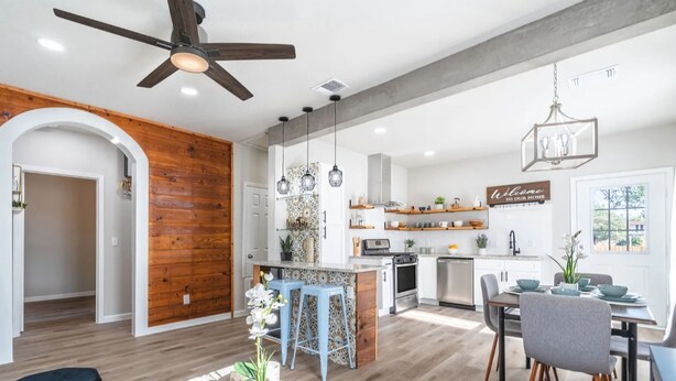 Una cocina moderna con una pared de acento de madera, un comedor con mesa y sillas, y un ventilador de techo.