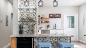 Una cocina con un salpicadero decorativo, un cartel de bienvenida y una encimera con taburetes.
