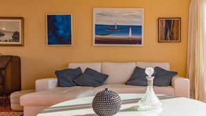 Un salon avec un canapé beige, des coussins foncés et une table basse blanche agrémentée d’objets décoratifs.