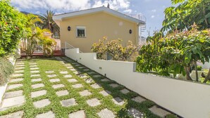 Une maison avec un jardin dallé, un mur blanc et diverses plantes.