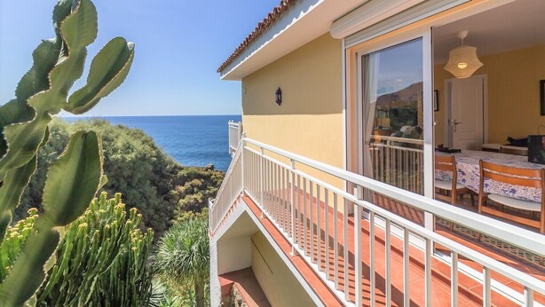 Une propriété située en bord de mer, dotée d’un balcon donnant sur l’océan, d’un coin repas avec une table et des chaises, et offrant une vue sur la mer.