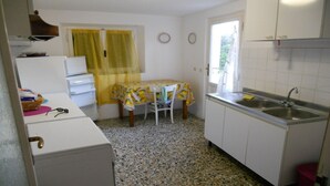 Een kleine keuken met een spoelbak, een tafel met een citroenkleurig tafelkleed, en een koelkast.