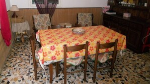Een eethoek met een tafel bedekt met een bloemig tafelkleed, omringd door houten stoelen. De vloer heeft een mozaïektegelpatroon.