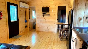 Interior de una cabaña de madera con cocina, una mesa de comedor y un televisor montado en la pared.