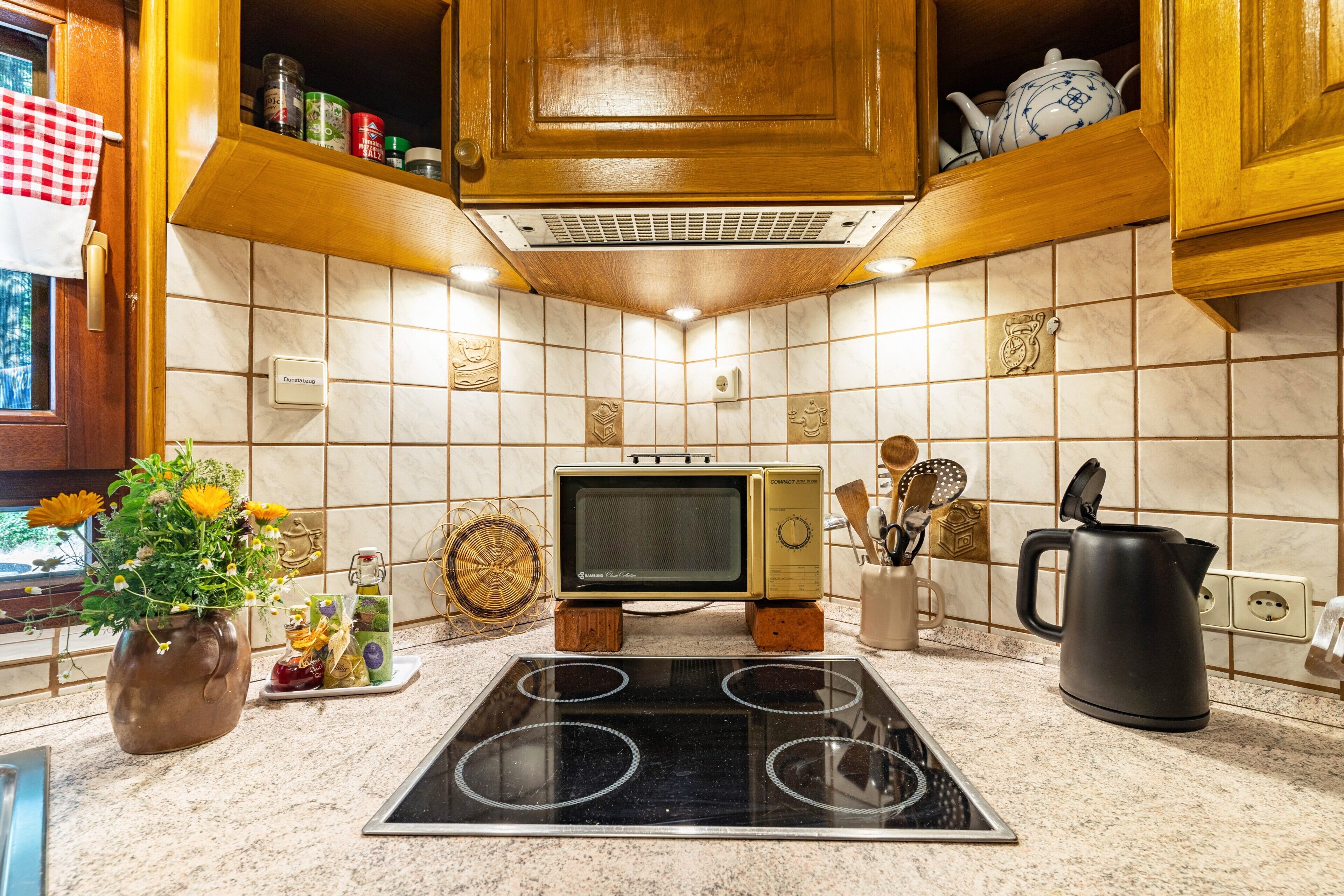 Une cuisine équipée d’un four à micro-ondes, d’une cuisinière, de meubles en bois et d’un vase de fleurs.