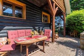 Une cabane en rondins avec une table et des chaises en bois, un canapé à carreaux rouges et une fenêtre avec un cadre jaune.