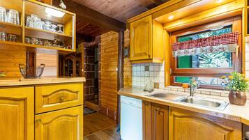 A wooden interior with a kitchen area, including a sink, cabinets, and a window with a checkered curtain.