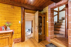 Un intérieur en bois avec un escalier en bois, une armoire aux portes vitrées et une petite table sur laquelle se trouvent des livres et un vase.