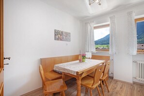 A dining area with a wooden table, chairs, a bench, a painting on the wall, and a window with a view of mountains.