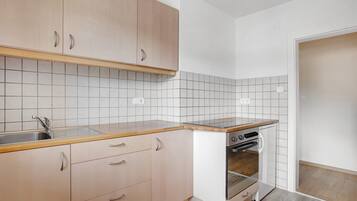 Una cocina con armarios de madera clara, un lavamanos de acero inoxidable, horno empotrado y salpicadero de azulejos blancos.