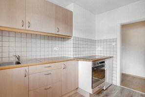 A kitchen with light wooden cabinets, a stainless steel sink, a built-in oven, and white tiled backsplash.