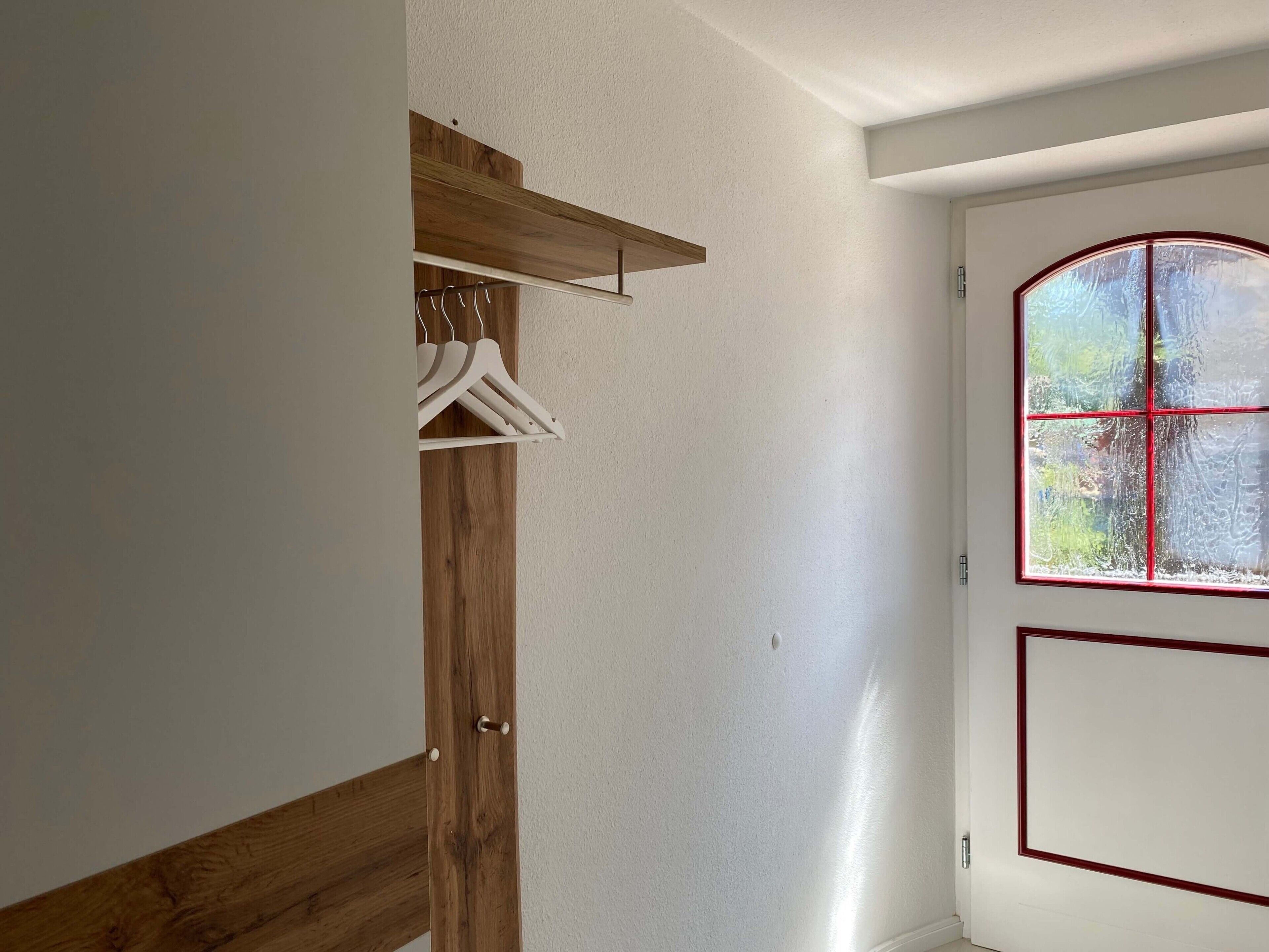 A room with a wooden wardrobe, a coat rack, and a door with a window.