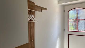 A room with a wooden wardrobe, a coat rack, and a door with a window.