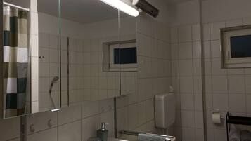 Een badkamer met een witte wastafel, een spiegel, een douche en een toilet.