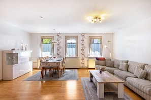 A living room with a sofa, a dining table with chairs, and a kitchen area with cabinets and a refrigerator.