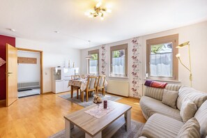 Un salon avec un canapé, une table à manger et des chaises, une table basse et, au fond, un coin cuisine.